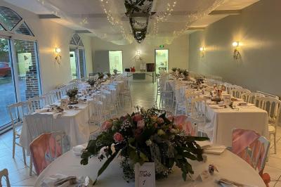 Centre de table avec bouquet de fleurs blanches et roses, numéro de table ’1’ et bougies sur une nappe blanche.