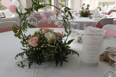 Centre de table avec bouquet de fleurs blanches et roses, numéro de table ’1’ et bougies sur une nappe blanche.