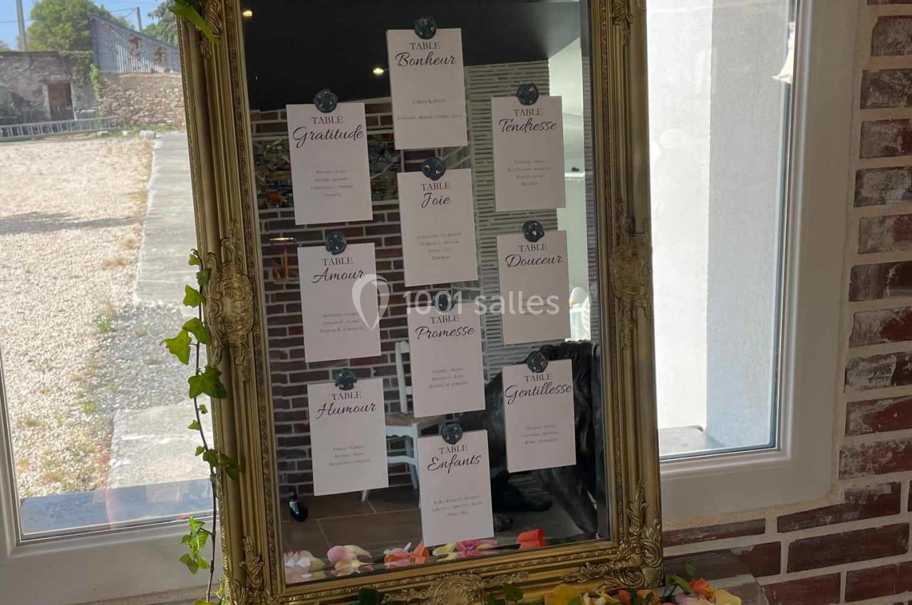 Cadre doré avec des cartes nominatives accrochées, posé sur une table décorée de pétales de fleurs et de lierre.