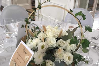 Centre de table avec bouquet de fleurs blanches et roses, numéro de table ’1’ et bougies sur une nappe blanche.