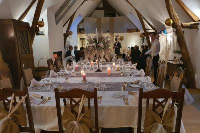 Table élégamment dressée avec nappes blanches, chaises assorties, chandeliers, fleurs roses et couverts dorés.
