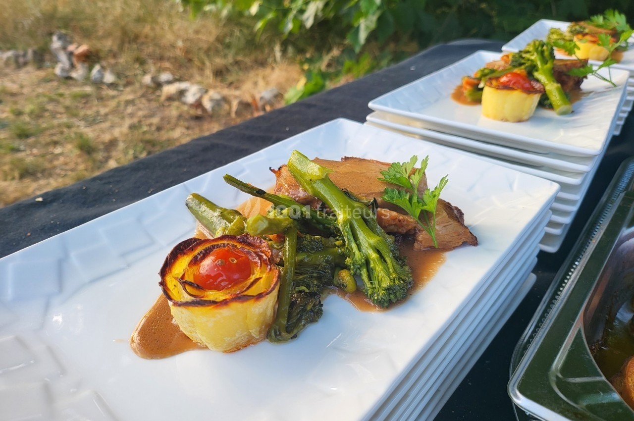 Assiette gastronomique avec viande, brocolis, roulé de pomme de terre et sauce, servie en extérieur.