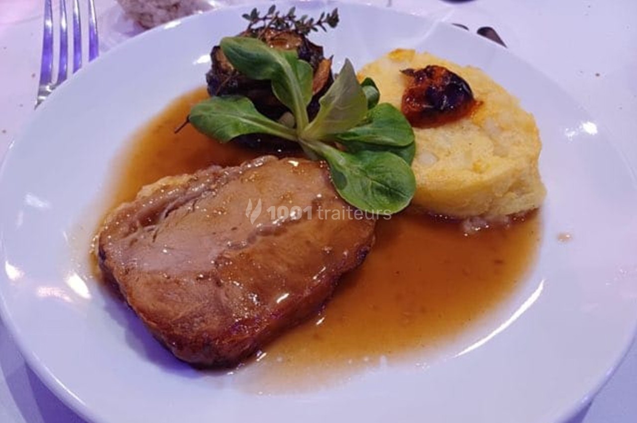 Assiette contenant une tranche de viande en sauce, purée, légumes grillés et garniture de feuilles vertes.