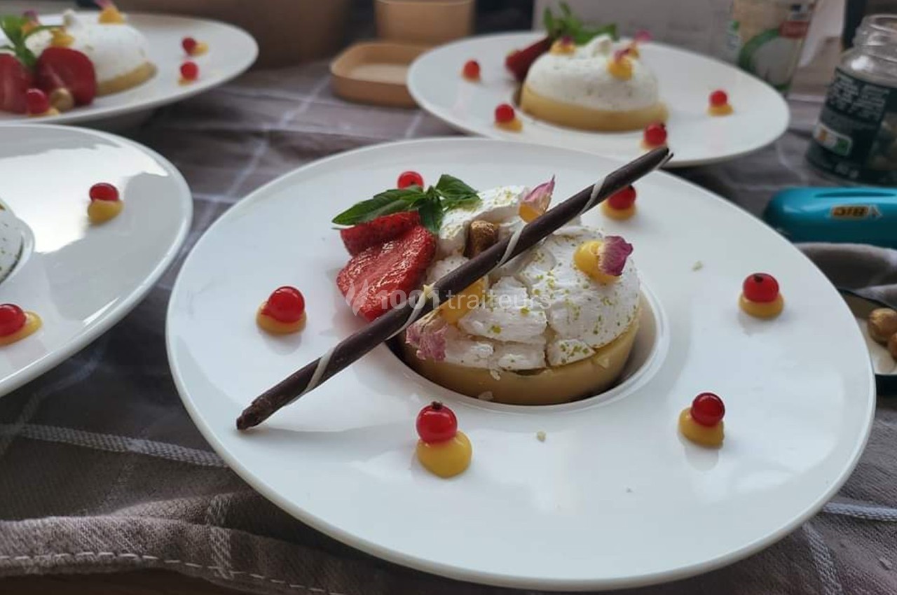 Assiette de dessert composée de mousse blanche, fraises, groseilles, crème jaune et décoration en chocolat.