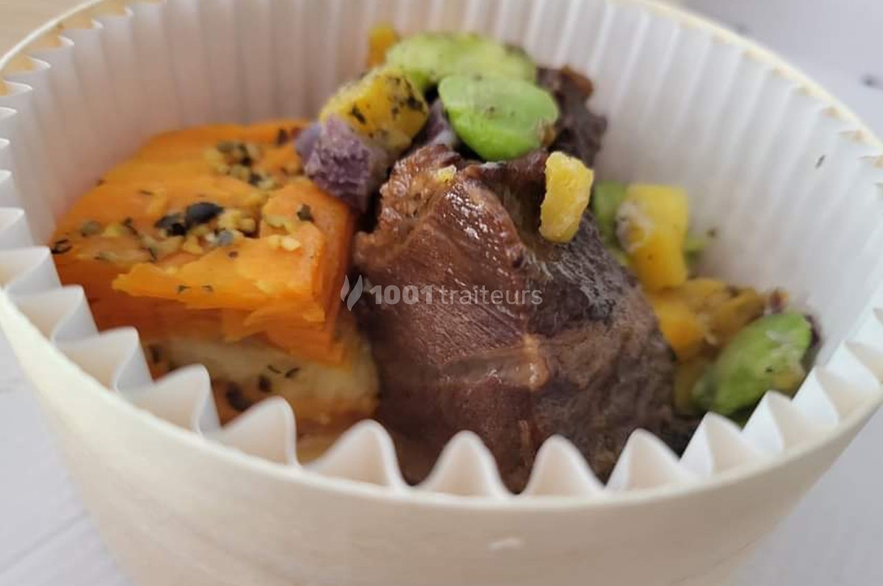 Plat servi dans un contenant en carton, composé de viande, patate douce, fèves et morceaux de légumes colorés.
