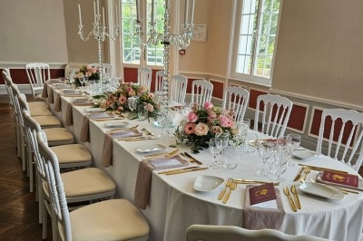 Table élégamment dressée avec nappes blanches, chaises assorties, chandeliers, fleurs roses et couverts dorés.