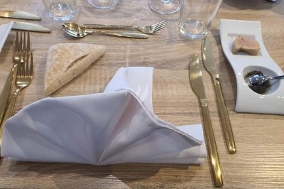 Table dressée avec nappe orange, couverts, verres, bouteilles et assiettes, disposée pour un repas ou une réunion.