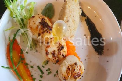 Table élégamment dressée avec nappes blanches, chaises assorties, chandeliers, fleurs roses et couverts dorés.