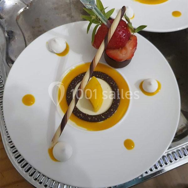 Assiette de dessert composée d'une mousse, d'un coulis de mangue, d'une décoration au chocolat et de fruits frais.