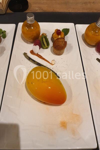 Dessert en forme de mangue avec décorations de fruits, sauce et pâtisseries sur une assiette blanche.