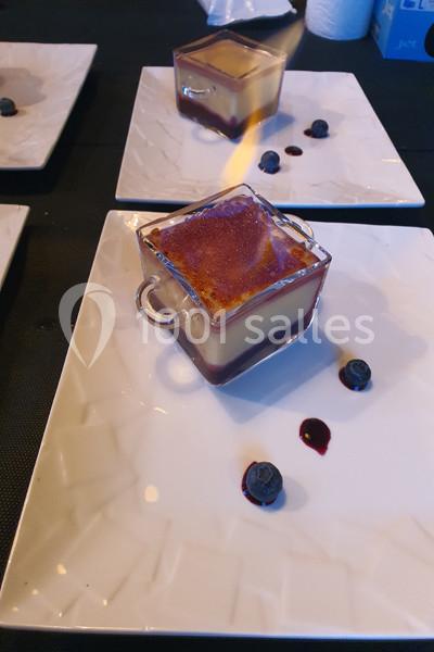 Dessert servi dans un verre carré avec une couche caramélisée, accompagné de myrtilles sur une assiette blanche.