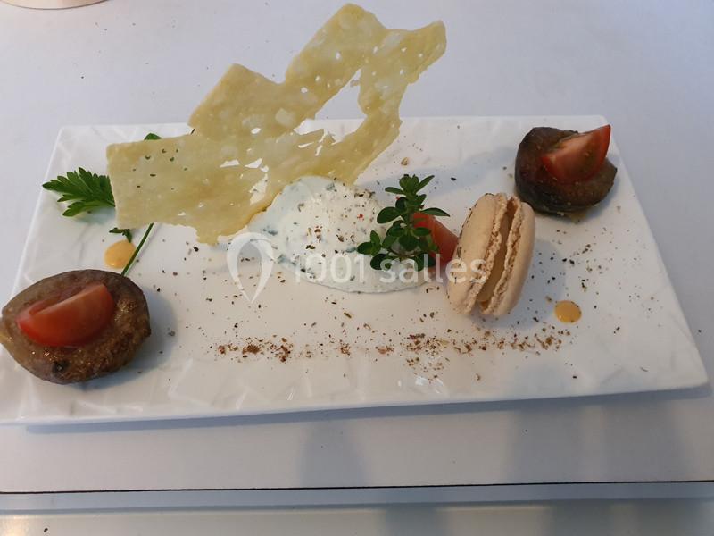 Assiette composée d'une mousse blanche, d'un macaron salé, de légumes grillés et d'une tuile fine en décoration.
