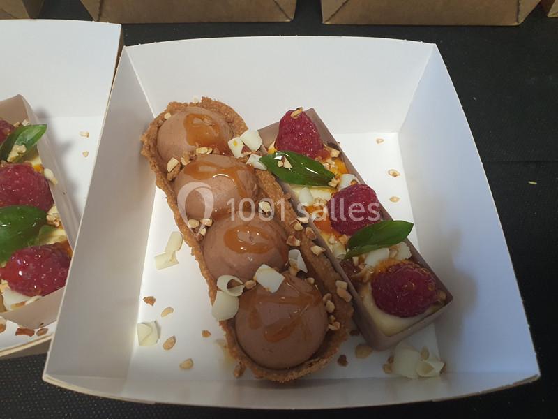 Pâtisserie composée de mousse au chocolat, framboises fraîches, feuilles de basilic et éclats d'amandes dans un écrin blanc.