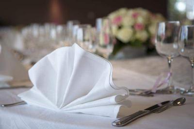 Table élégamment dressée avec nappes blanches, chaises assorties, chandeliers, fleurs roses et couverts dorés.