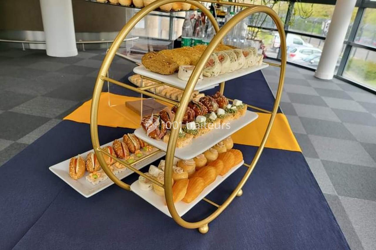 Présentoir doré avec trois étages de viennoiseries, pains et amuse-bouches disposés sur des assiettes blanches.