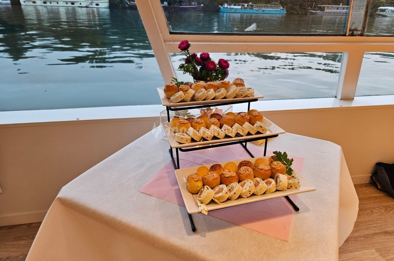 Plateau de petits pains garnis disposés sur un présentoir à trois niveaux, avec vue sur une rivière en arrière-plan.