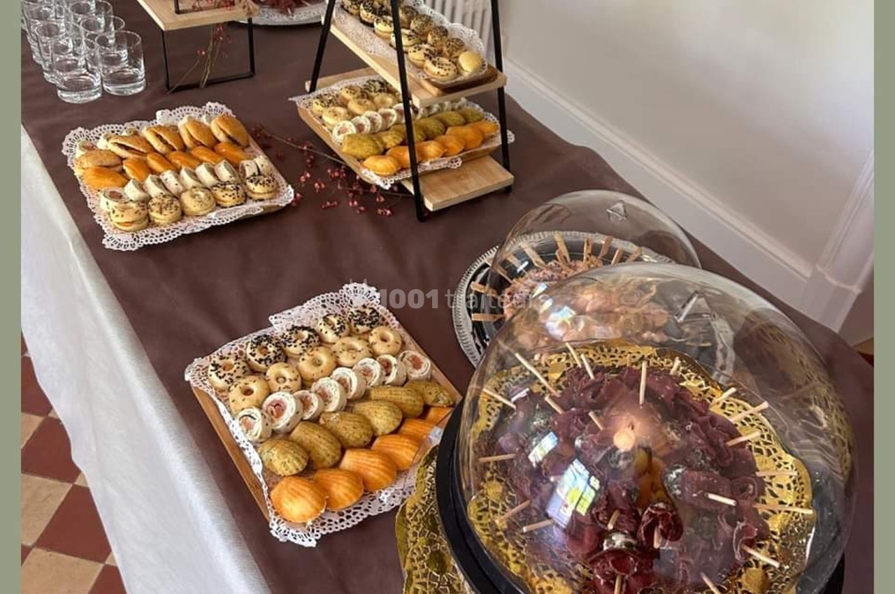 Table garnie de pâtisseries variées, verrines et charcuteries sous cloche, disposées sur une nappe marron.