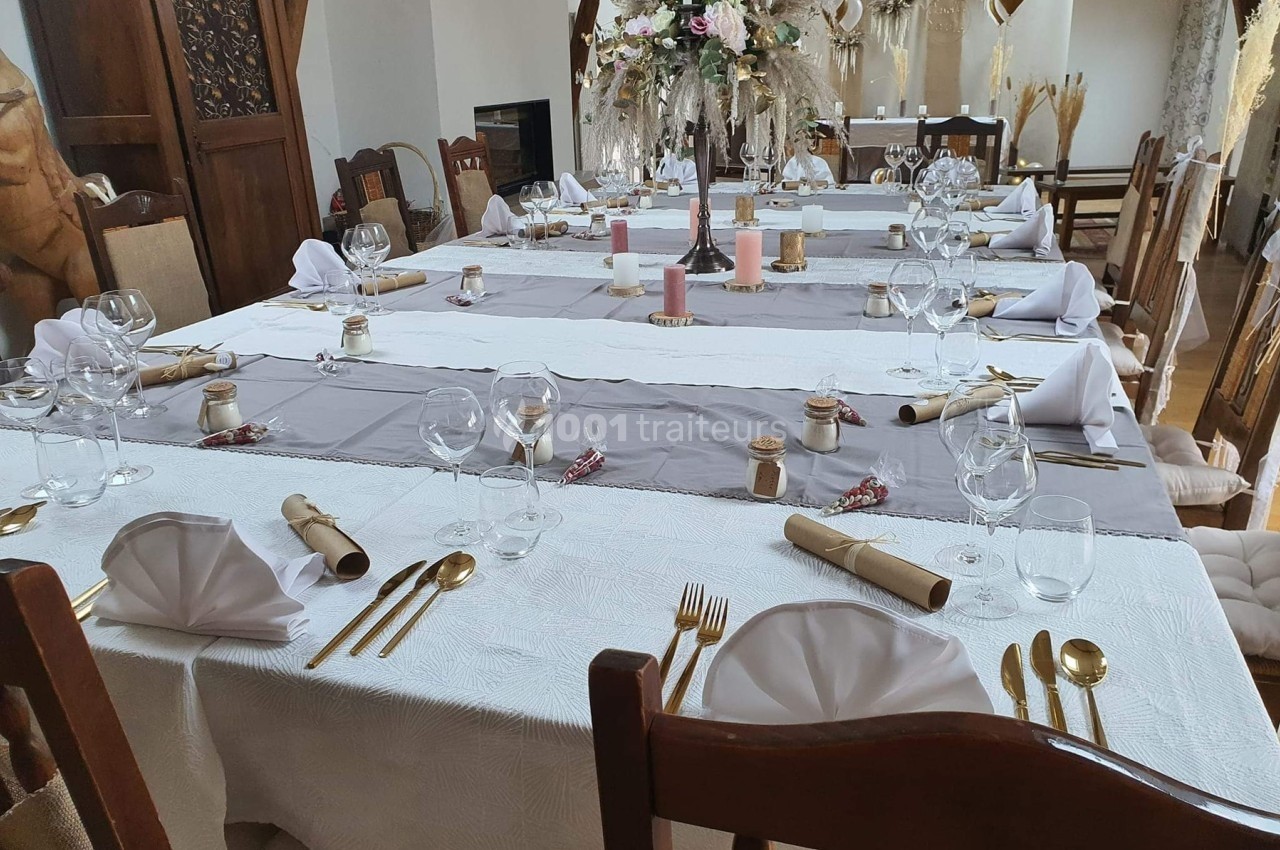 Table dressée pour un repas festif avec nappes blanches et grises, couverts dorés, serviettes pliées et décoration florale.