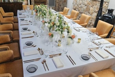 Table dressée avec nappe orange, couverts, verres, bouteilles et assiettes, disposée pour un repas ou une réunion.
