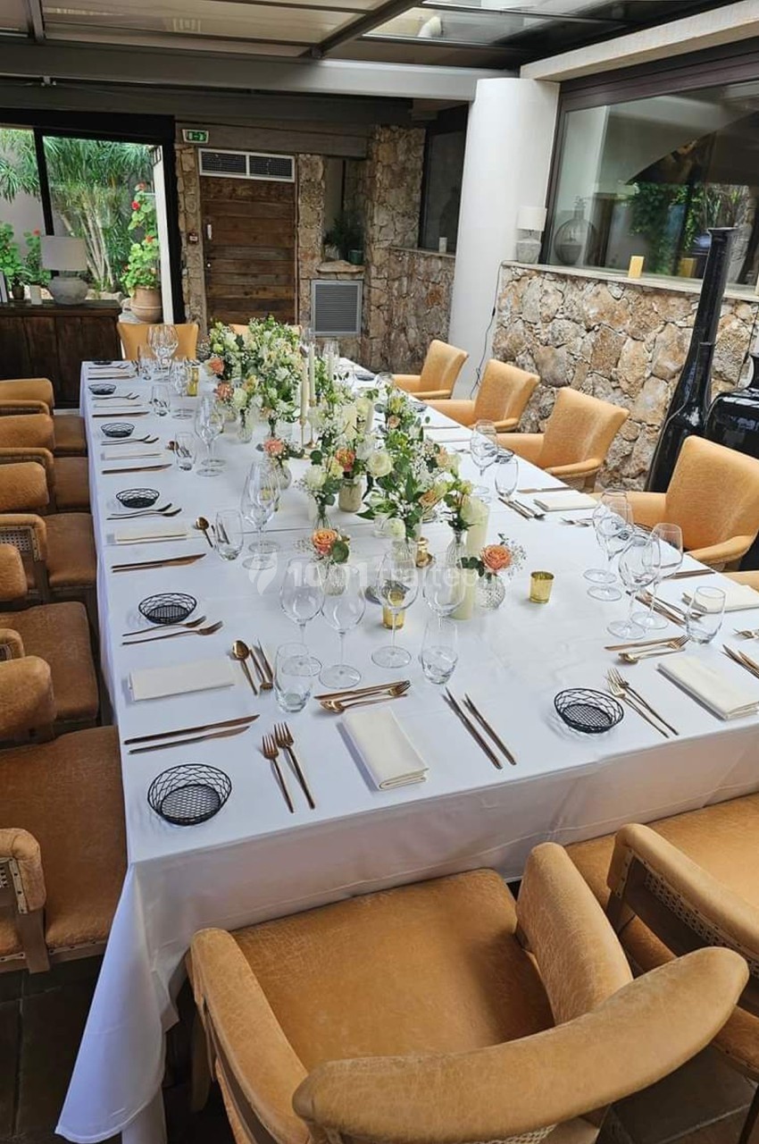 Table dressée pour un repas, ornée de fleurs et de bougies, entourée de chaises en bois dans une salle lumineuse.