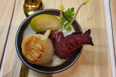 Table dressée avec nappe orange, couverts, verres, bouteilles et assiettes, disposée pour un repas ou une réunion.