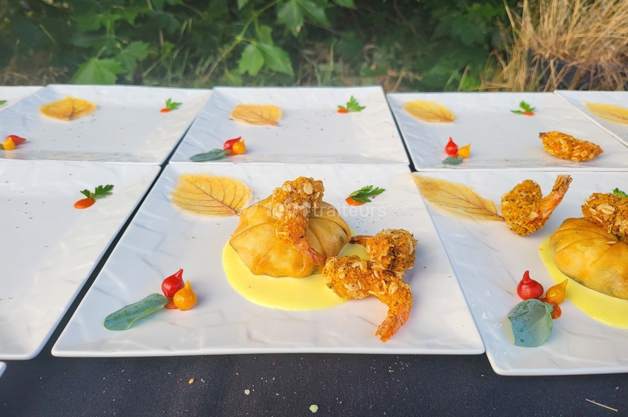 Assiette gastronomique avec croustillant, crevettes panées, purée et décorations colorées sur une table en extérieur.
