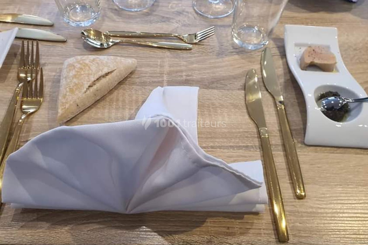 Table dressée avec couverts dorés, serviette pliée, pain, et assiette contenant du foie gras et une sauce.