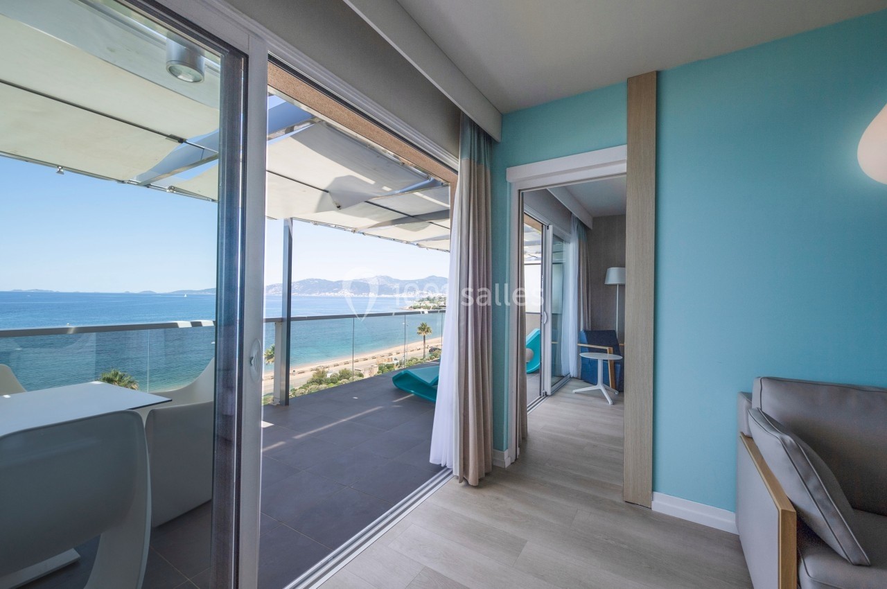 Vue depuis une chambre lumineuse avec balcon donnant sur la mer, équipée de mobilier moderne et terrasse ombragée.