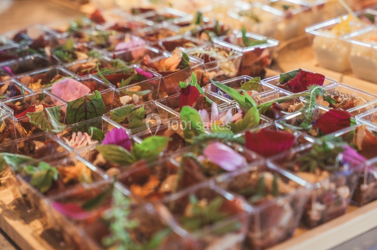 Assortiment de verrines garnies de fleurs comestibles, herbes fraîches et ingrédients variés sur une table.