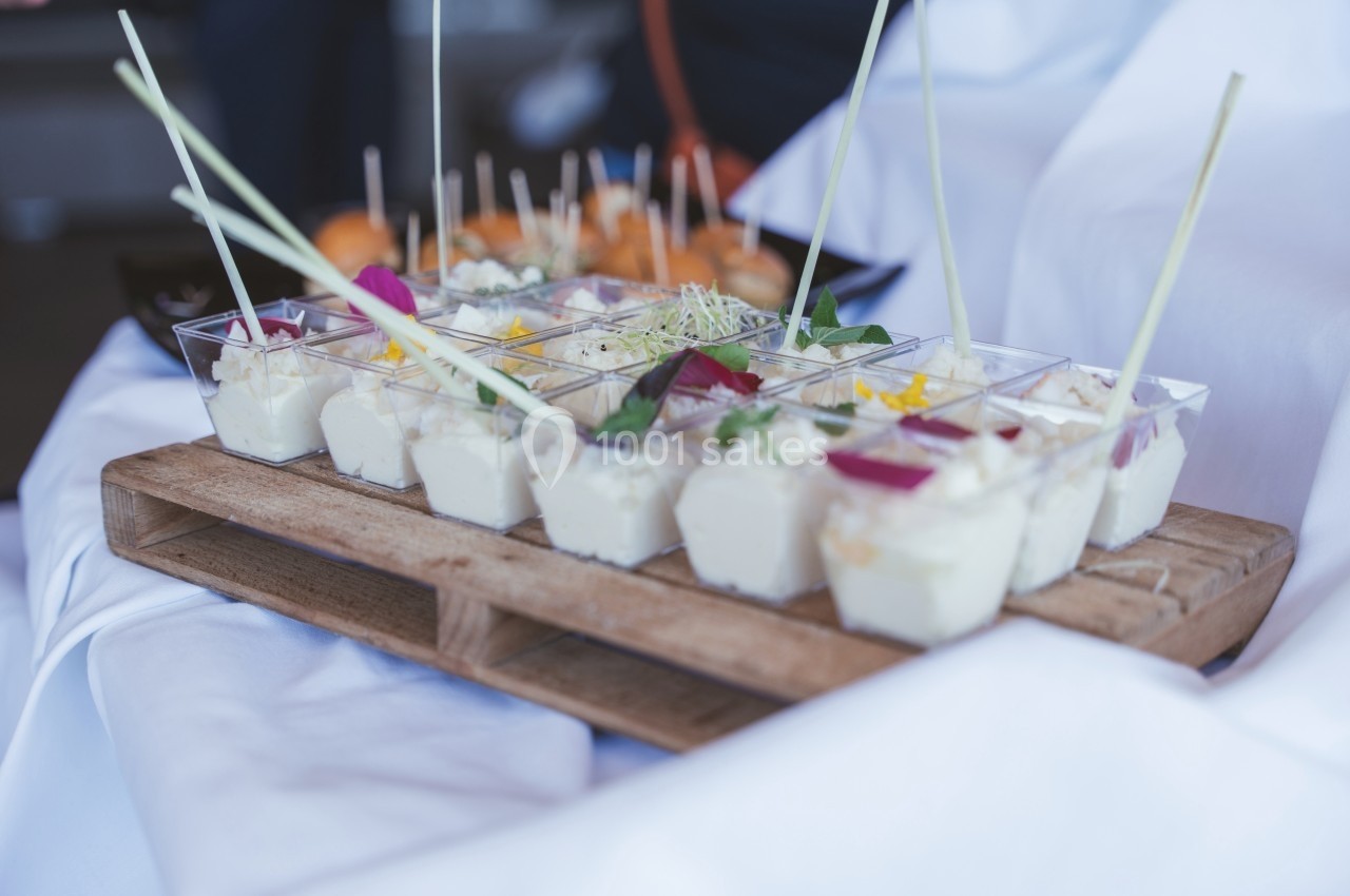 Plateau en bois avec verrines de mousse blanche garnies de fleurs comestibles et herbes, présenté sur une nappe blanche.