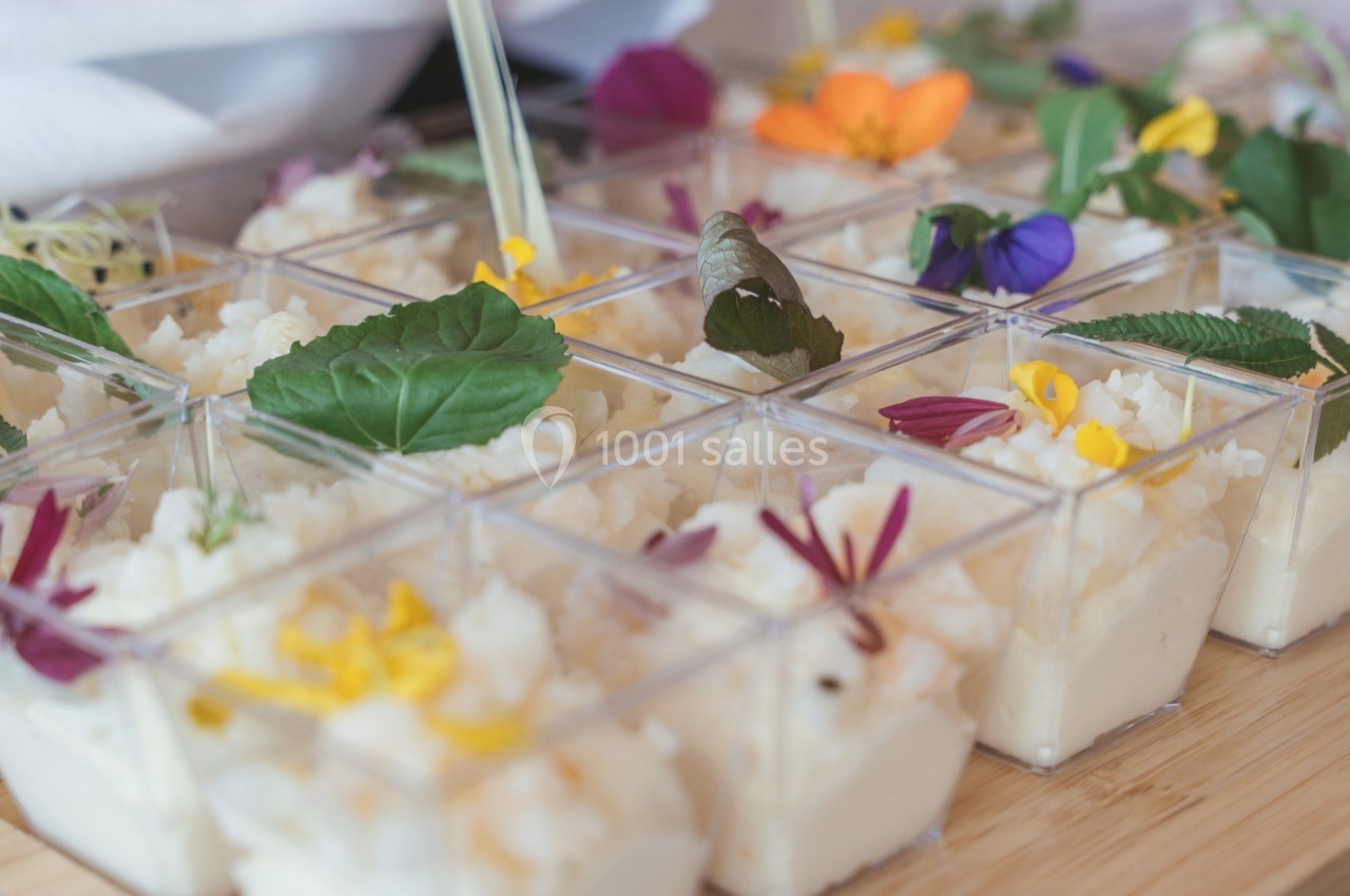 Petits verrines de mousse blanche garnies de fleurs comestibles colorées sur une table en bois.