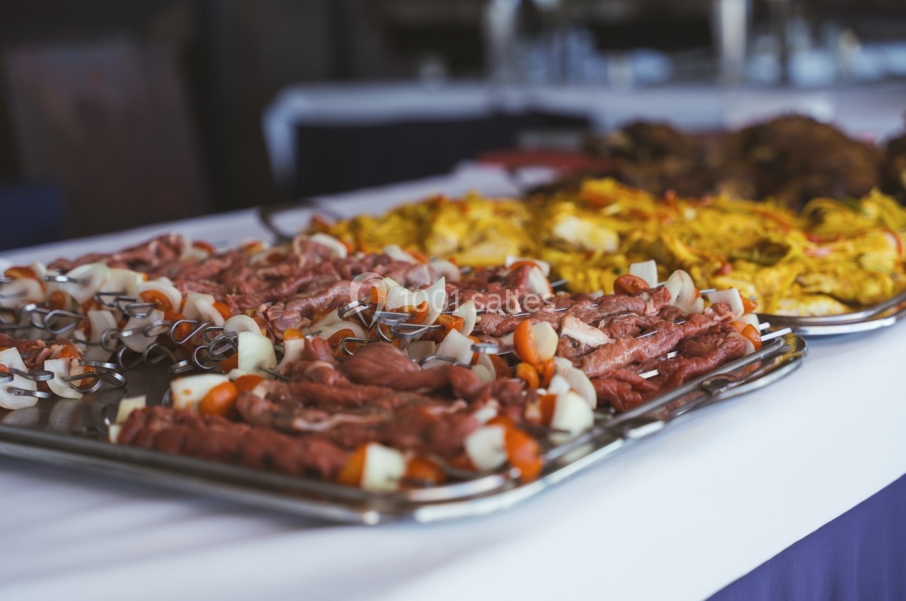 Plateaux de brochettes de viande crue et de riz safrané présentés sur une table lors d'un buffet.