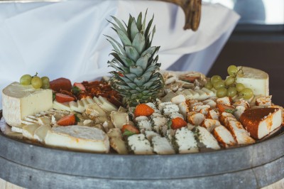 Plateau de fromages variés avec des fruits, dont des raisins, des fraises et un ananas au centre, présenté sur un tonneau.
