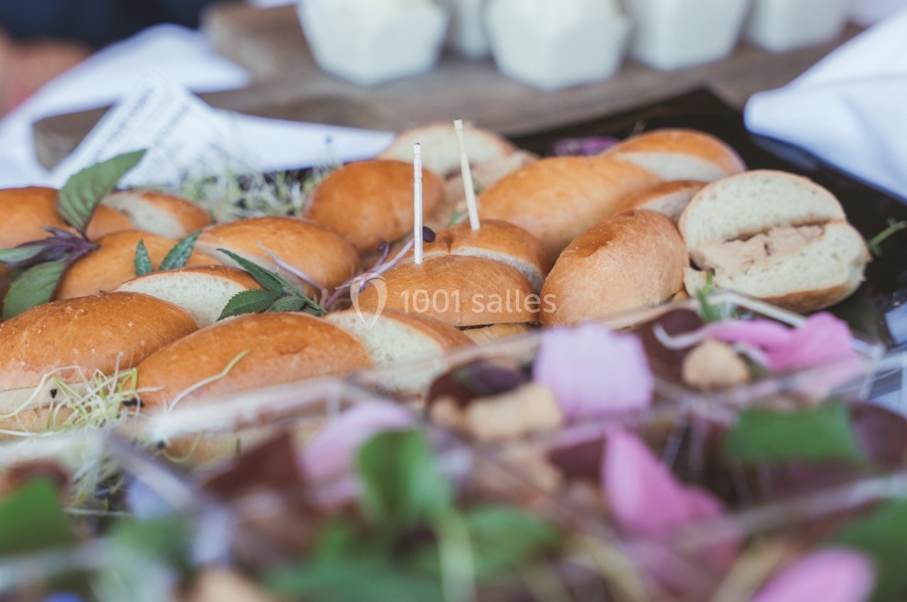 Plateau de petits sandwichs garnis, entouré de décorations végétales et d'autres plats en arrière-plan.