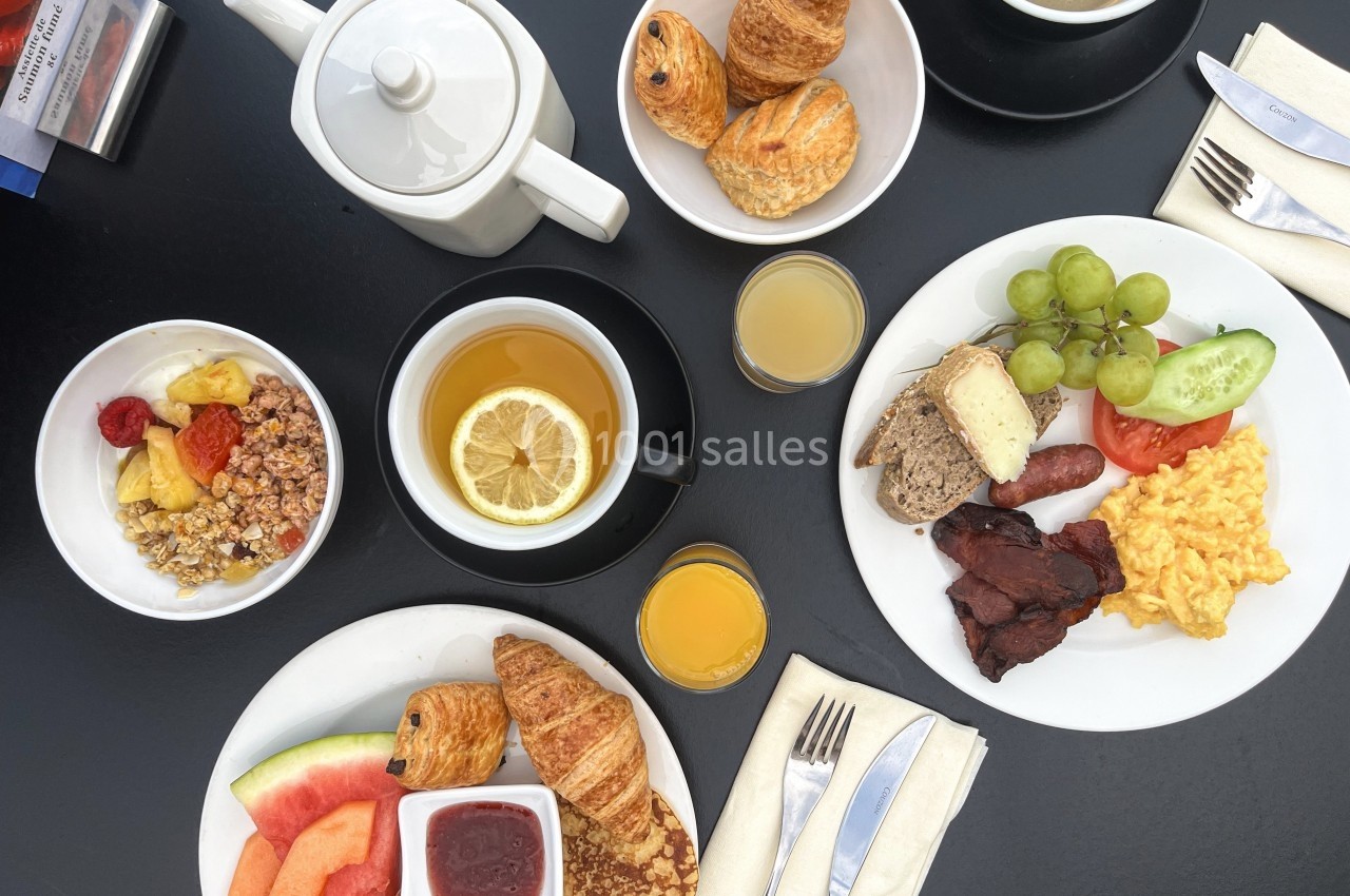 Petit-déjeuner varié avec croissants, fruits, céréales, œufs brouillés, charcuterie, thé, café et jus d'orange.