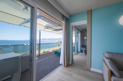 Chambre lumineuse avec lit double, mobilier moderne et vue sur la mer depuis une grande baie vitrée.