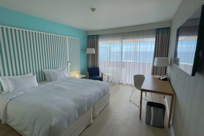 Chambre lumineuse avec lit double, mobilier moderne et vue sur la mer depuis une grande baie vitrée.