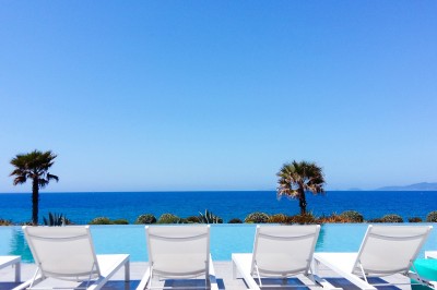 Chambre lumineuse avec lit double, mobilier moderne et vue sur la mer depuis une grande baie vitrée.
