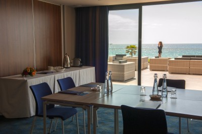 Chambre lumineuse avec lit double, mobilier moderne et vue sur la mer depuis une grande baie vitrée.
