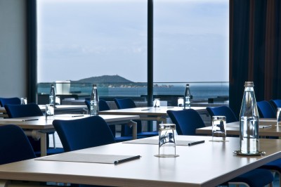 Chambre lumineuse avec lit double, mobilier moderne et vue sur la mer depuis une grande baie vitrée.