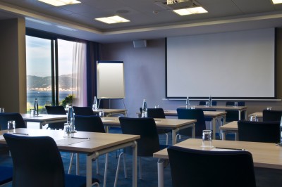 Chambre lumineuse avec lit double, mobilier moderne et vue sur la mer depuis une grande baie vitrée.