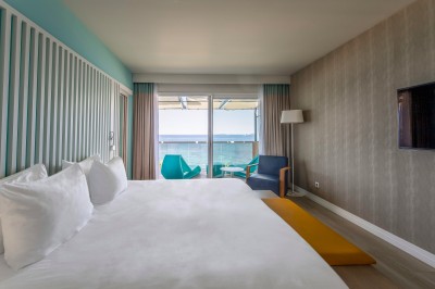 Chambre lumineuse avec lit double, mobilier moderne et vue sur la mer depuis une grande baie vitrée.