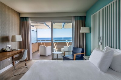 Chambre lumineuse avec lit double, mobilier moderne et vue sur la mer depuis une grande baie vitrée.