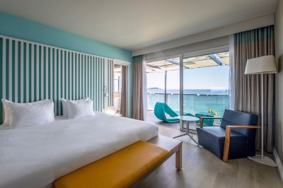 Chambre lumineuse avec lit double, mobilier moderne et vue sur la mer depuis une grande baie vitrée.