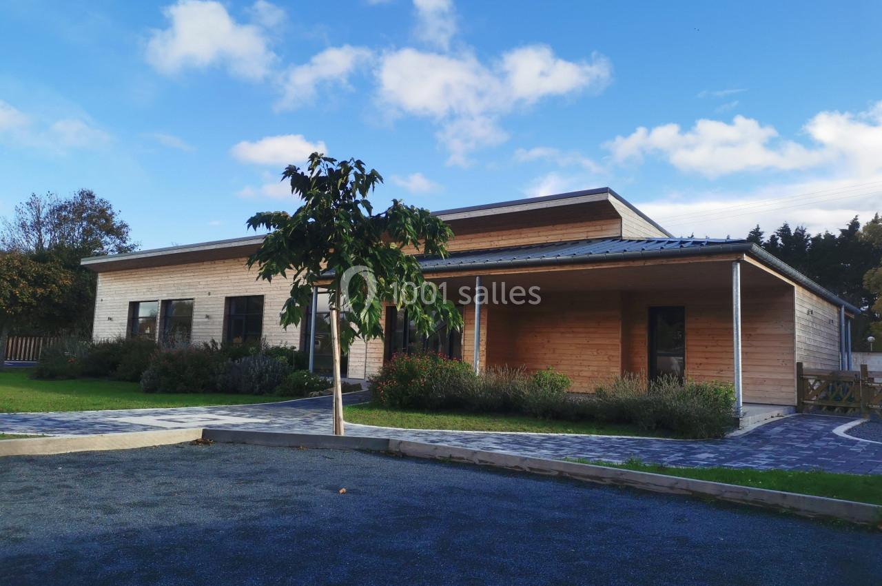 Maison en bois moderne avec un toit plat, entourée de verdure et d'un chemin pavé sous un ciel bleu.