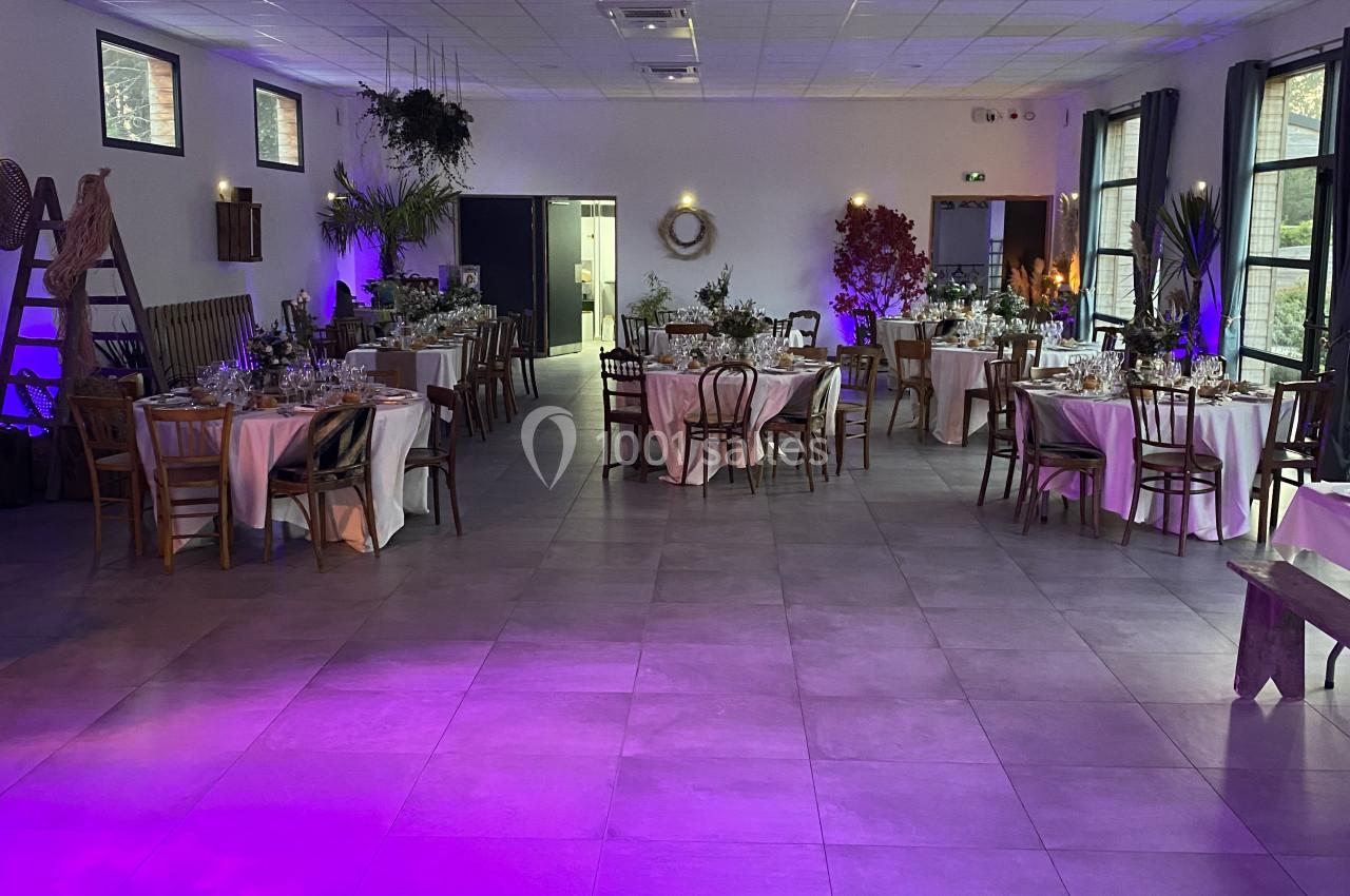 Salle de réception décorée avec des tables dressées, éclairage tamisé et ambiance lumineuse violette.