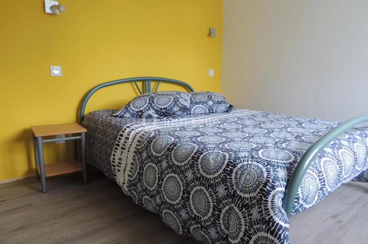 Lit double avec une structure métallique grise, draps à motifs circulaires et mur jaune en arrière-plan.