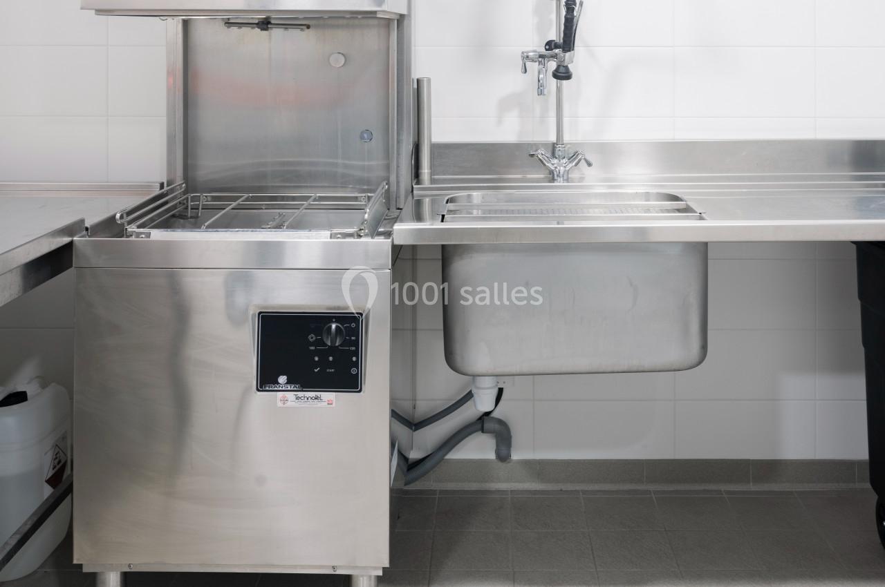 Lave-vaisselle professionnel en acier inoxydable à côté d'un évier dans une cuisine équipée.