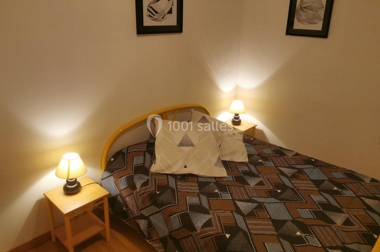 Lit avec une housse géométrique, encadré par deux tables de chevet avec lampes allumées, dans une chambre sobre.