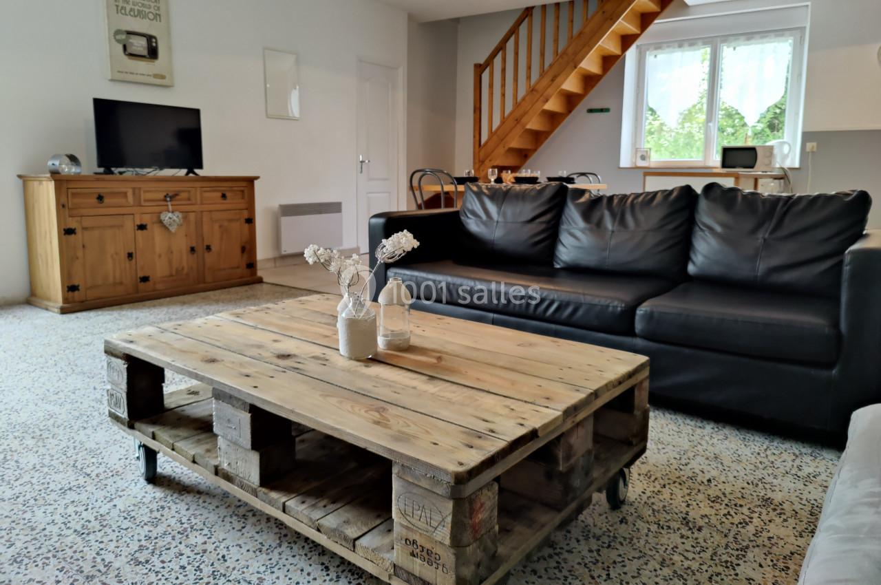 Salon avec canapé en cuir noir, table basse en palettes, buffet en bois et escalier menant à l'étage.